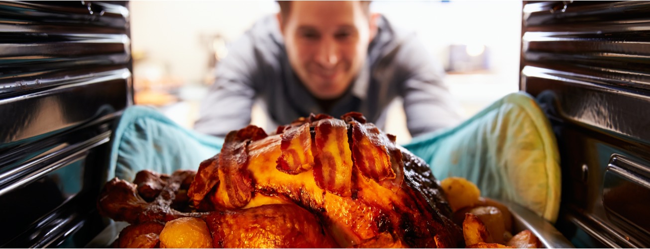 Man pulling bacon wrapped turkey out of oven