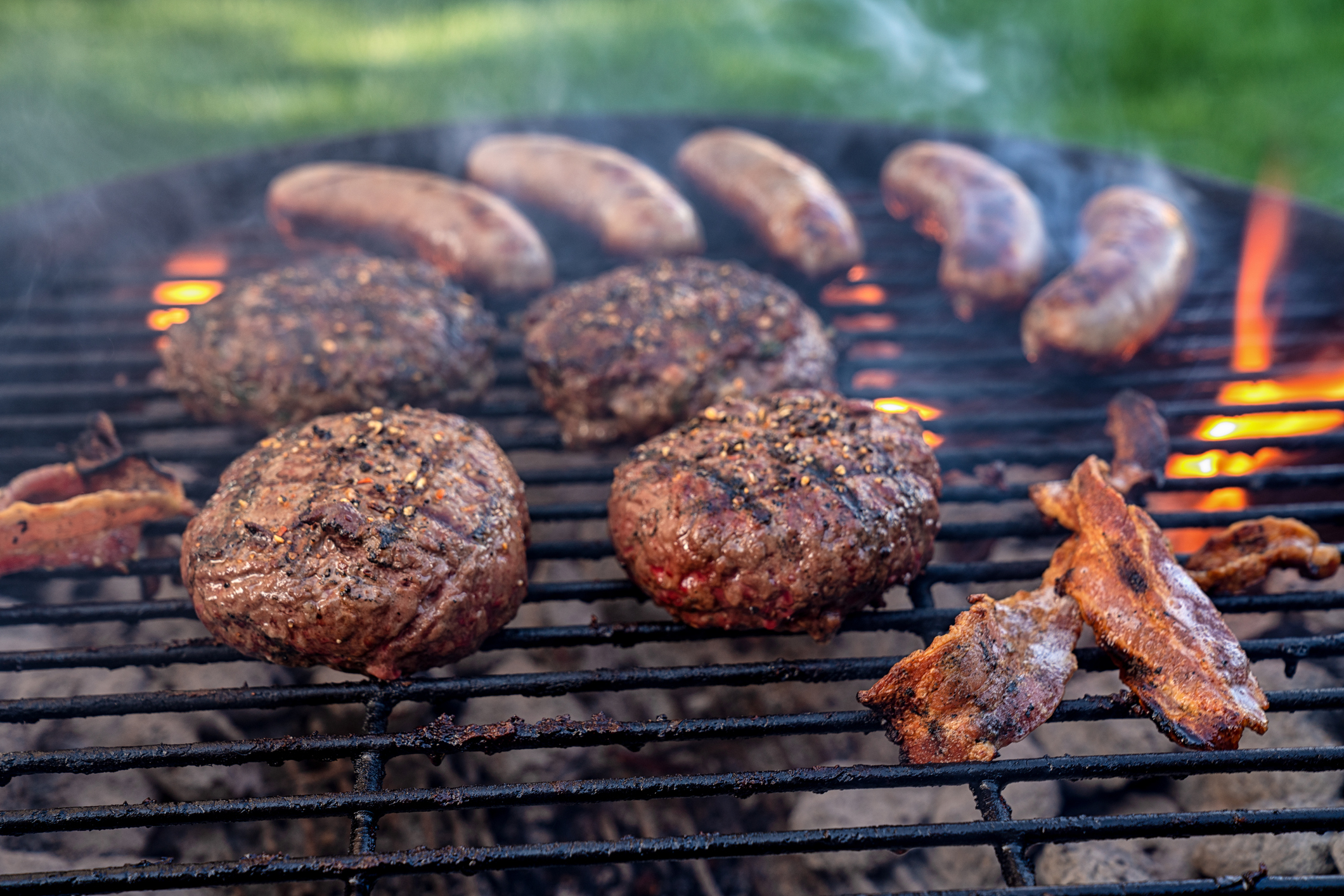 Burgers, bacon and sausage been grilled